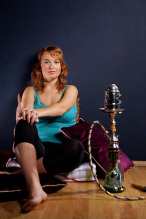 Young woman in style of hippie smoking hookah in interior location like room or house.
