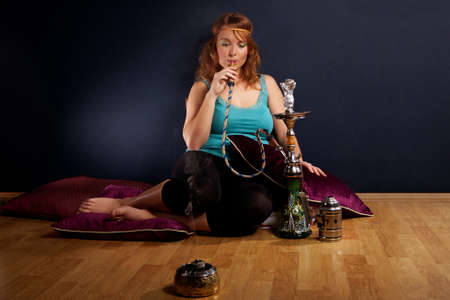 Young woman in style of hippie smoking hookah in interior location like room or house.