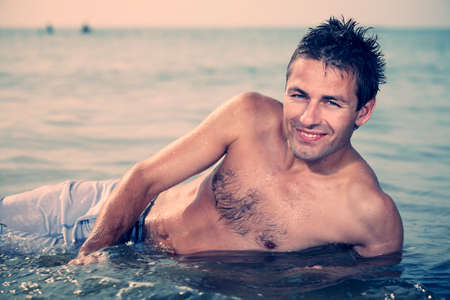 Young man posing on Italian bech in water and relaxing in summer sun.の写真素材