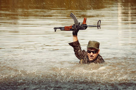 Soldier in uniform swimming in lake with assault rifle