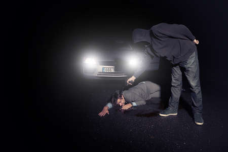 Masked murderer shooting man in suit in front of car on routeの写真素材