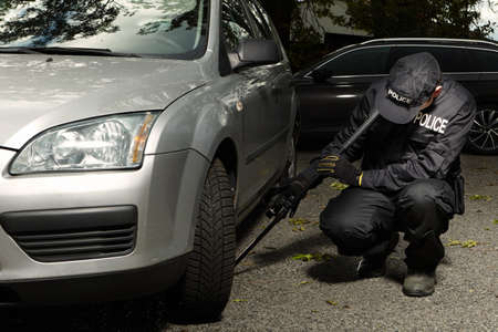 Police officer checking car floor with inspection mirror for threats of bombs