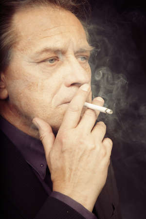 Aging Caucasian man smoking tobacco cigarette on black background