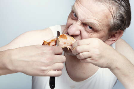 Aging man in an a-shirt cutting a piece of chicken with a razor.の写真素材