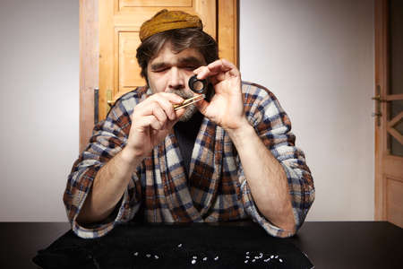 Old fashioned diamond smuggler watching stones with magnifier