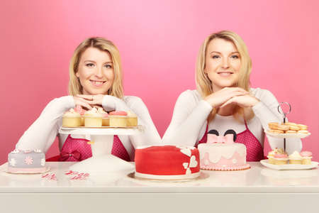 Nice blonde twins baking cakes posing with their sweetsの写真素材