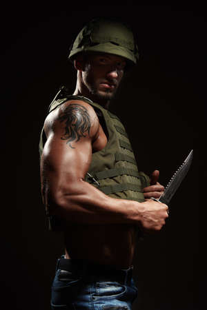 Muscle hero man in tactical vest armed with survival knifeの写真素材