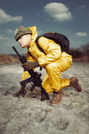 Freak gunman afraid of atomic war in yellow overall going noticeably through landscape