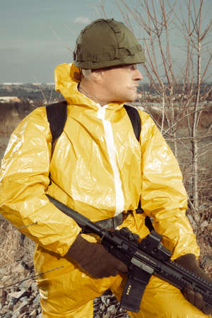 Freak gunman afraid of atomic war in yellow overall going noticeably through landscape