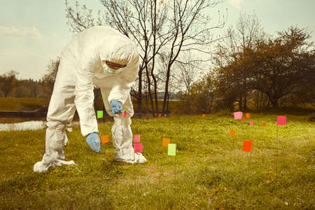 Criminologist technician working on tracing of evidences in terrain with flags
