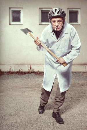 Older paramedic freak man in medical coat and protective helmet attacking with double axeの写真素材