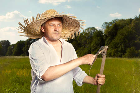 Village natural country man on summer meadow sharpening scythe with sharpening stone