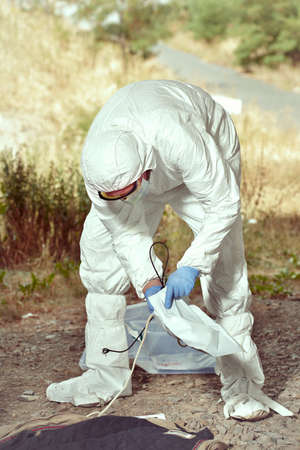 Criminologist technician in  free protective suit collecting evidences of probable criminal actの写真素材