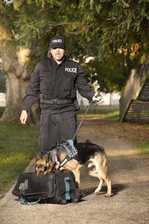 Police officer with his dog checking unknown potentially dangerous bag in park