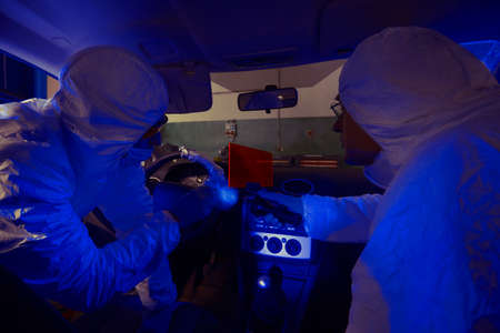 Crime investigation - looking for evidences and traces in suspected car in police garage under UV...