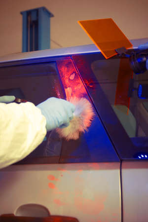 Crime investigation - developing of fingerprints on suspected car in police garage under UV light