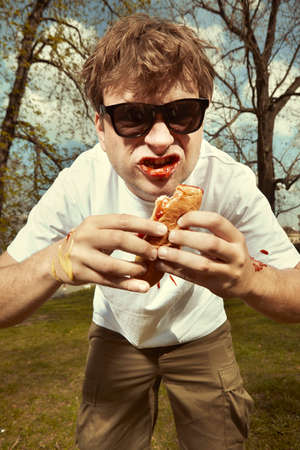 Man in street park eating hot dog with mustard, ketchup and dough bun