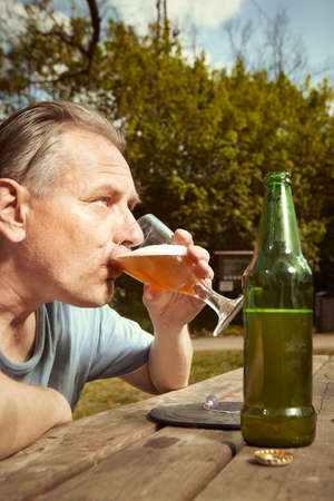 Older man in summer park drinking beer after spiritual connection with ghosts