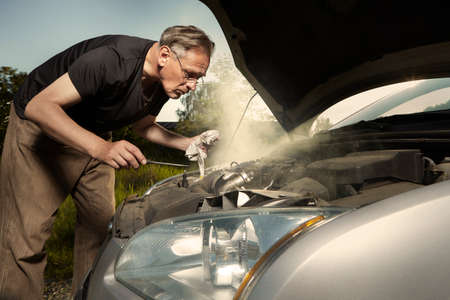 Aging man trying to fix broken car engine on lonely way