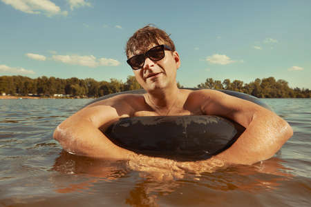 Funny man in sunglasses swimming in lake on inner tube