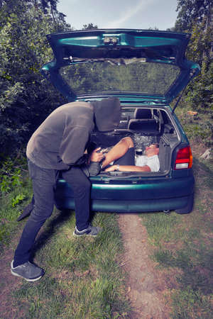 Addicted criminal pulling killed man on forest way to carの写真素材