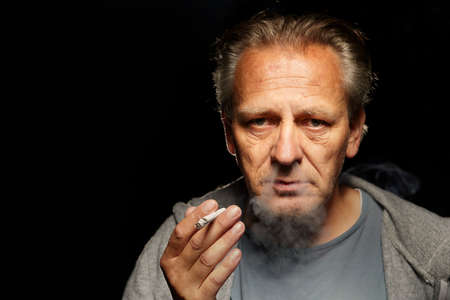 Older caucasian man smoking cigarette on dark background