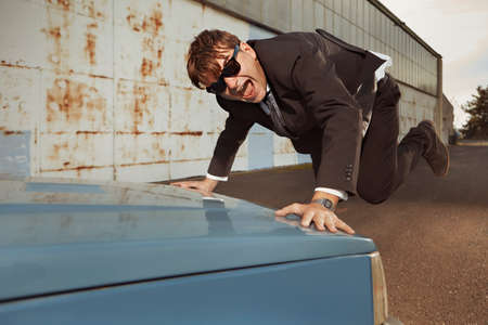 Angry man in black suit destroying his lovely retro car