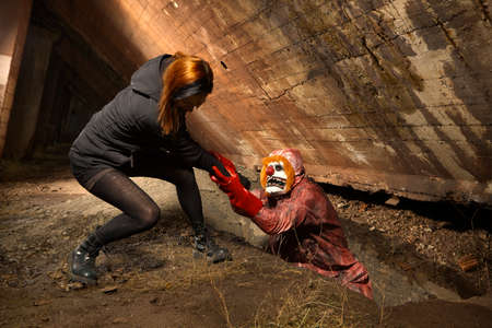 Scary clown man in nightmare style attacking young woman