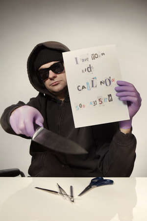 Criminal in hooded shirt preparing ransom letter from newspaper