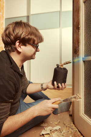 Man at home removing havy layer of old paint from door with burnerの写真素材