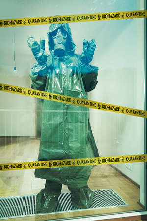 Ugly man in empty apartment behind barrier tape dressed to protective suit and maskの写真素材