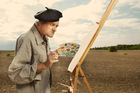 Older man painting artwork on canvas in sunny day fieldの写真素材