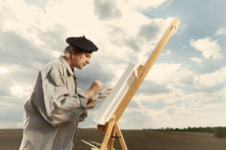 Older man painting artwork on canvas in sunny day fieldの写真素材
