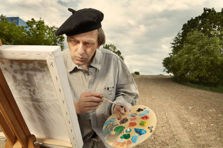 Older man painting artwork on canvas in sunny day fieldの写真素材