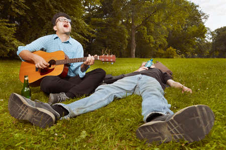 Two men on city park summer meadow enjoying day with guitar