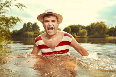 Funny man in stylish retro swimsuit and straw hat swimming in river