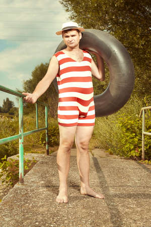 Funny man in stylish retro swimsuit and straw hat posing with inner tubeの写真素材