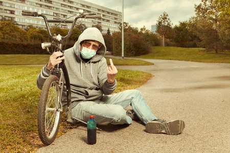 Older city man vagabond in hooded shirt with mask on scooterの写真素材