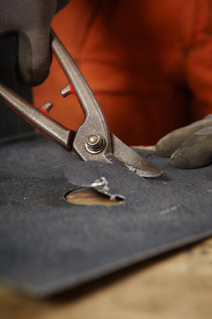 Hand shearing round hole in sheet metal roof components in workroomの写真素材