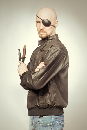 Man fighter with throwing knives posing in studio with eye patch on faceの写真素材