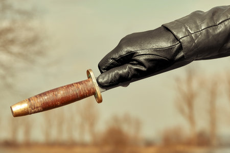 Detail of throwing knife holding in hand dressed in leather glove