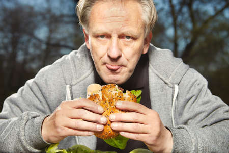 Man in public city park enjoying and eating his hamburger meal