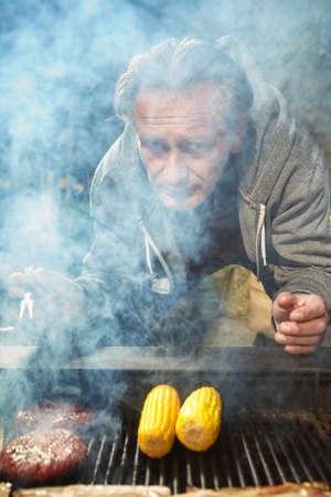 Man in public city park grilling beef hamburger patties for his mealの写真素材