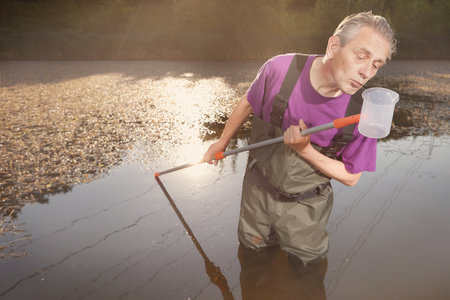 Water quality analyst dressed in chest wader collecting samplesの写真素材