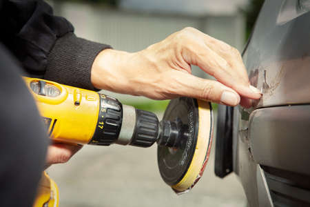 Man in overall working with drill on damage of his car directly on streetの写真素材