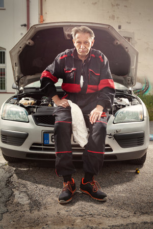 Man in overall working on open engine of his car directly on streetの写真素材