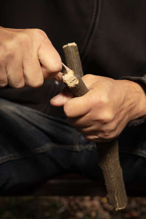 Details of slingshot making of wooden fork by older man in black hooded shirtの写真素材