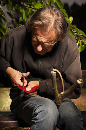 Older man finishing traditional slingshot of wooden forkの写真素材