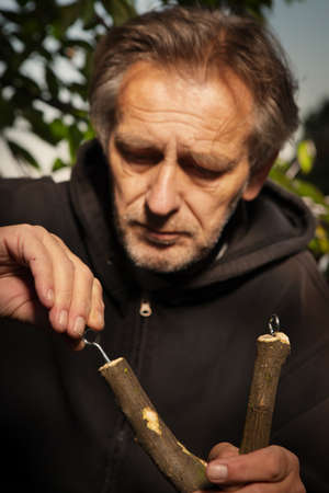 Details of slingshot making of wooden fork by older man in black hooded shirtの写真素材