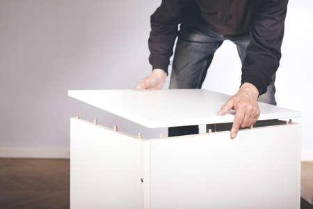 Man assembling set of three laminated wooden drawers